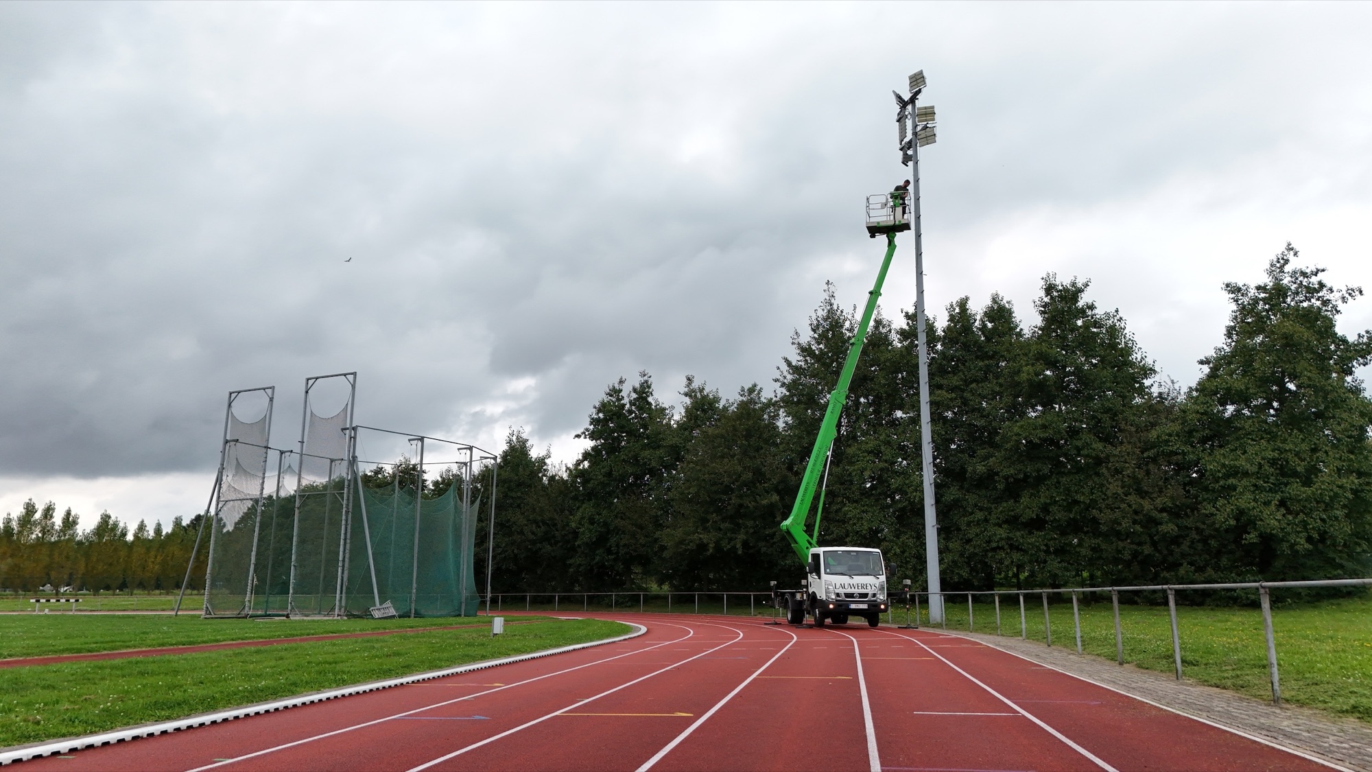 Technicus werkt aan de lichtmast langs de atletiekbaan