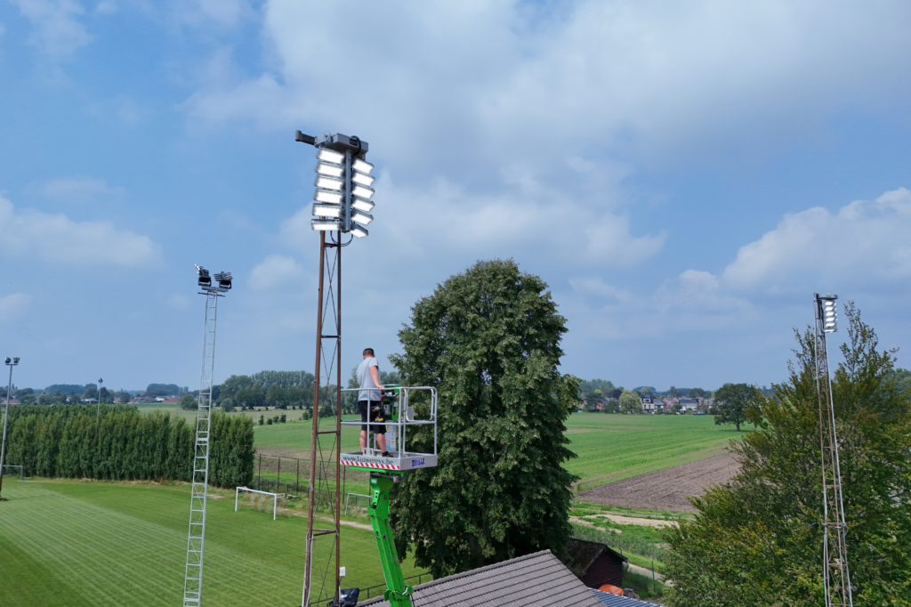 Technicus installeert LED-armaturen op een verlichtingsmast met hoogtewerker op een buitenterrein.