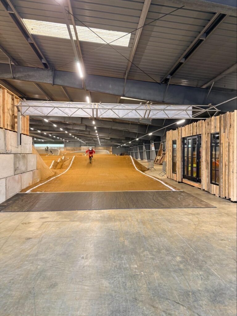 Close-up van de dakconstructie van een indoor BMX-hal met meerdere rijen lineaire LED-armaturen die zorgen voor gelijkmatige verlichting over het volledige parcours.